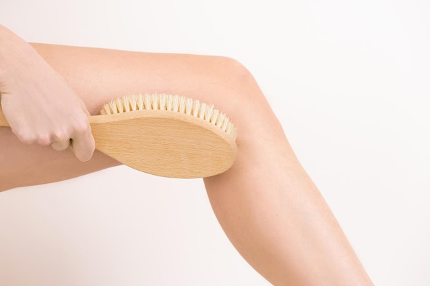 Femme massant la peau de sa jambe avec une brosse de massage sèche anti-cellulite peeling soins du corps gros plan