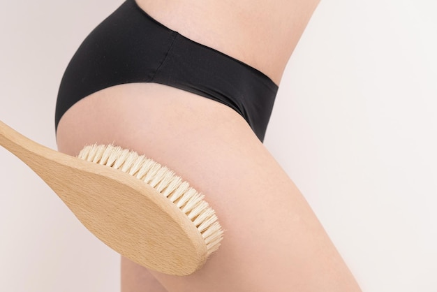 Femme massant la peau de sa jambe avec une brosse de massage sèche anti-cellulite peeling soins du corps gros plan