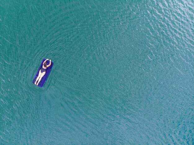 Femme sur matelas dans l'espace de copie de vue aérienne de l'eau azur