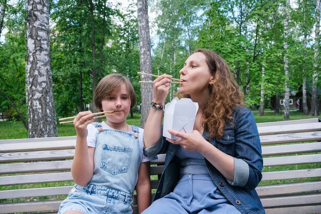 Une femme mature d'âge moyen et une adolescente en promenade un jour d'été dans le parc déjeunent avec des nouilles au wok