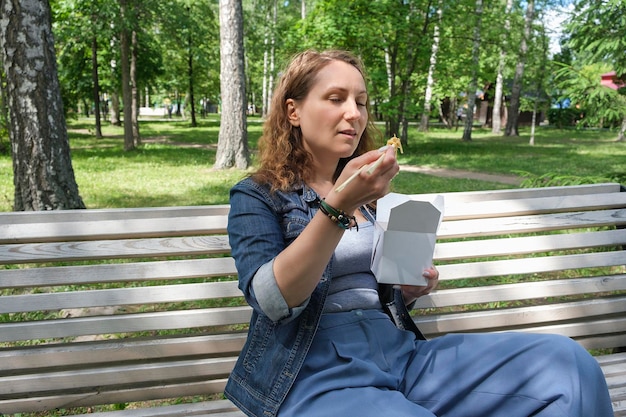 Une femme mature d'âge moyen lors d'une promenade un jour d'été dans le parc déjeune avec des nouilles au wok