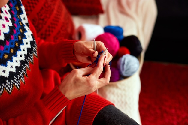 Femme mature assise dans un canapé confortable et tricotant tout en profitant du week-end à la maison, femme âgée tricotant, se détendre à la maison faire son activité de loisir préférée le week-end, concept de bien-être