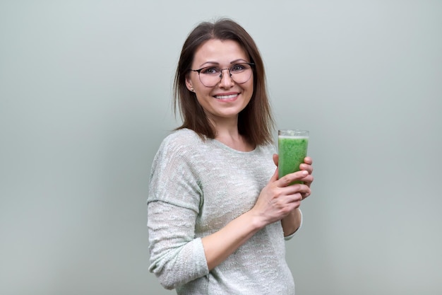 Femme mature avec boisson smoothie aux légumes verts, régime végétalien sain, espace de copie. Santé, alimentation, âge, antioxydant, végétarien, femme sur fond vert pastel