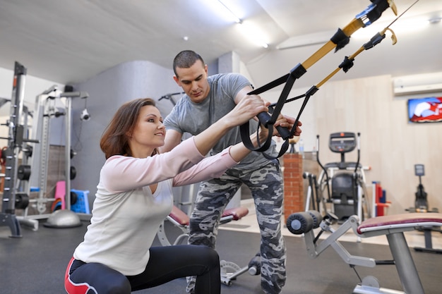 Femme mature exerçant dans la salle de gym à l'aide de boucles de sangles de fitness.