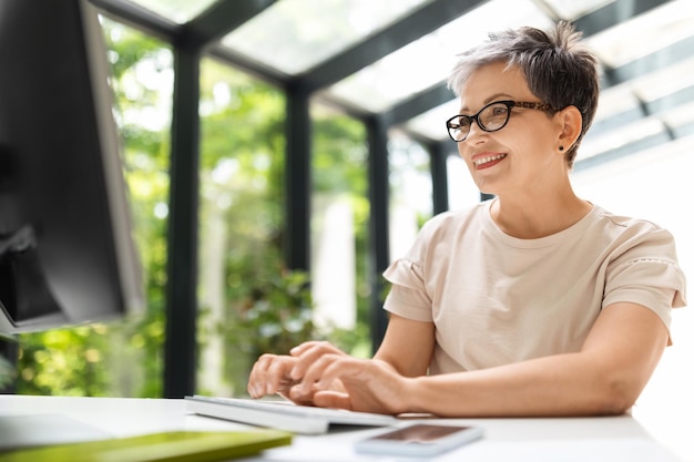 Une femme mature heureuse travaillant à distance depuis son bureau à domicile sur un PC.