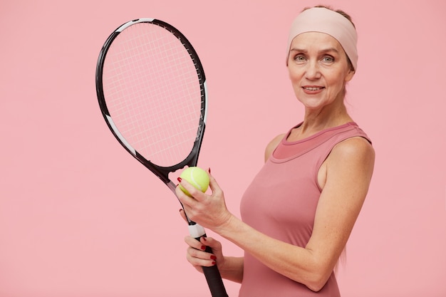 Femme mature jouant au tennis sur fond rose