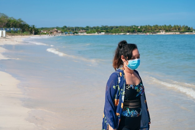 Femme mature avec masque de protection marche sur la plage
