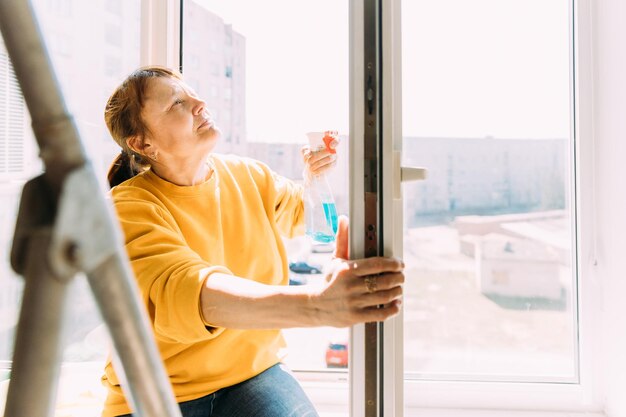 Photo une femme mature nettoie une fenêtre.