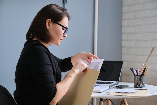 Femme mature ouvrant une enveloppe avec des documents papier