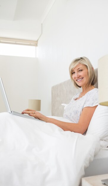 Femme mature souriante à l&#39;aide d&#39;ordinateur portable au lit