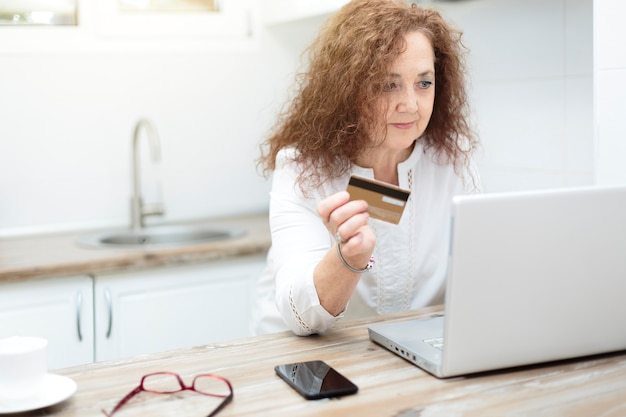 Femme mature tenant une carte de crédit et utilisant un ordinateur portable à la maison. Achats en ligne, commerce électronique et services bancaires par Internet à partir du concept de la maison.