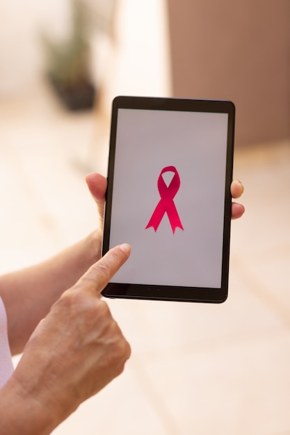 Femme mature tenant une tablette avec un ruban rose. Mois de sensibilisation au cancer du sein avec image technologique.