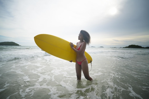 Femme mature transporte une planche de surf dans des vagues douces