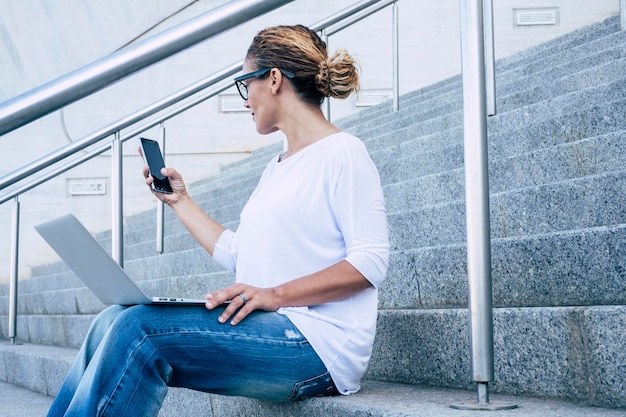 Photo une femme mature utilisant un téléphone portable et un ordinateur portable alors qu'elle est assise sur des marches