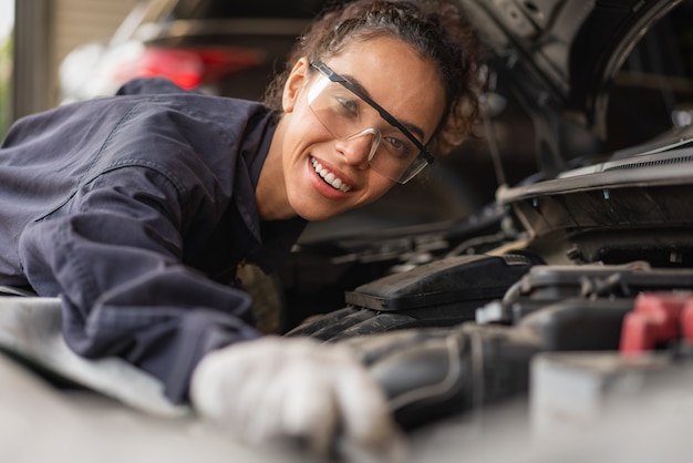 Photo femme mécanicien souriant et travaillant à l'entretien de réparation d'une voiture dans le garage de service automobile