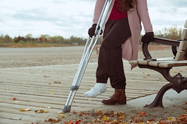 femme méconnaissable avec une blessure au pied utilisant des béquilles pour s'asseoir sur un banc