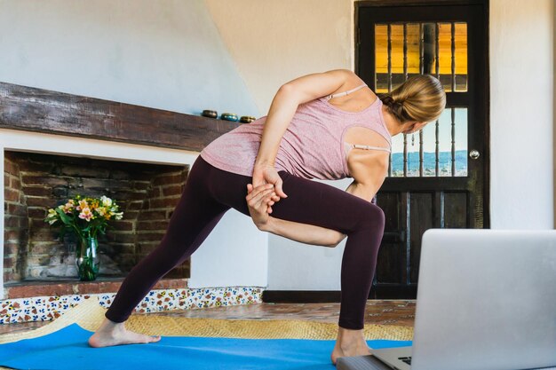 Photo femme méconnaissable dans un appartement effectuant une pose flexible pour un cours de yoga en ligne. bien-être mental.