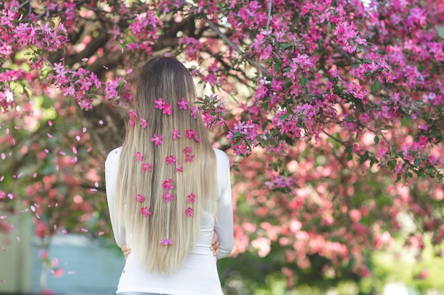 Femme méconnaissable, debout à l'arrière de la caméra avec de longs cheveux blonds avec des fleurs dans les cheveux. Femme sur fond de printemps. Dame à l'extérieur.