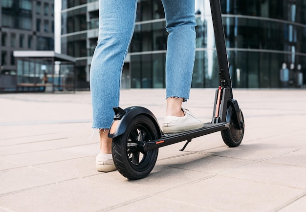 Une femme méconnaissable debout sur un scooter électrique dans la ville