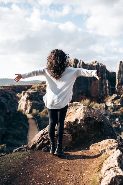 Femme méconnaissable étendant ses bras au vent au sommet d'un paysage naturel spectaculaire