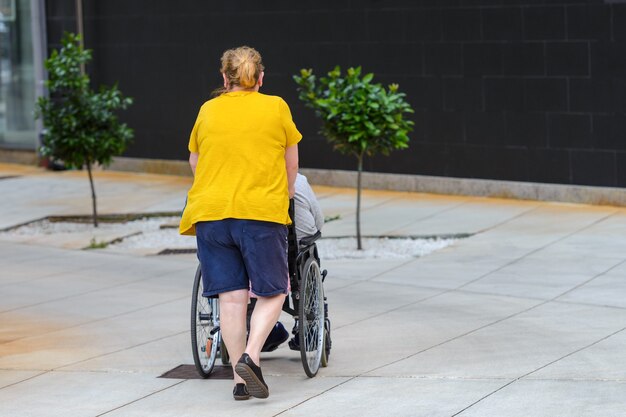 Femme Méconnaissable Poussant Un Fauteuil Roulant Avec Une Personne Handicapée, Vue Arrière