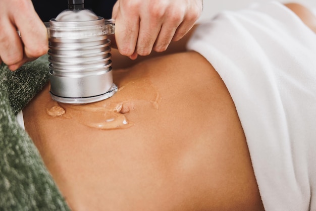 Femme méconnaissable recevant un traitement de cavitation par ultrasons pour réduire la graisse sur l'abdomen au salon de beauté.