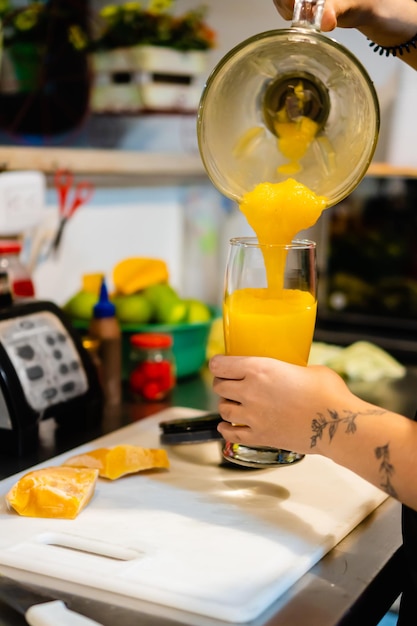 Femme méconnaissable serveuse dans un magasin local servant du jus de mangue avec une photo verticale de mélangeur