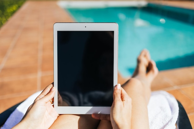 Femme méconnaissable travaillant avec une tablette au bord d'une piscine