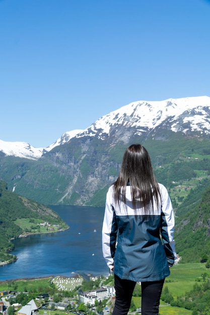 Femme méconnaissable avec une vue incroyable sur le Geirangerfjord en arrière-plan avec les montagnes enneigées et une journée ensoleillée