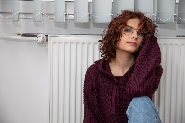 Une femme mécontente est assise près du chauffage en raison du manque de chaleur dans la maison.