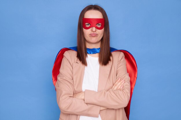 Une femme mécontente portant un costume de super-héros se tient isolée sur un fond bleu étant déçue exprimant sa tristesse en regardant la caméra avec un visage insatisfait