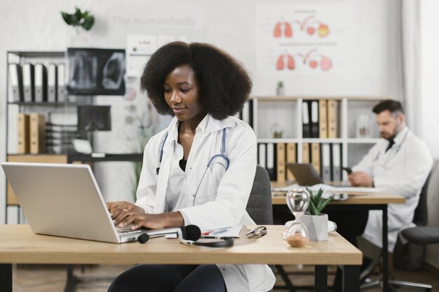 Femme médecin africaine assise au bureau et tapant sur un ordinateur portable