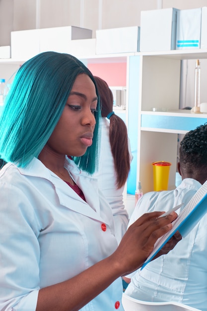 Femme médecin africaine, infirmière ou étudiante en médecine en blouse blanche lit des notes sur le bloc-notes. Jeune professionnel se prépare à travailler dans un laboratoire de test hospitalier pour analyser les échantillons de patients pour le coronavirus.