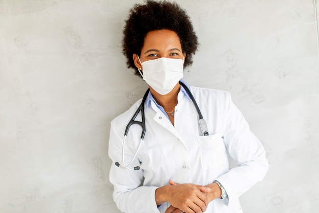 Une femme médecin afro-américaine porte un uniforme blanc et un masque facial protecteur à l'hôpital