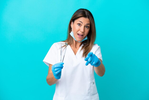 Femme médecin d'âge moyen isolée sur fond bleu surprise et pointant vers l'avant