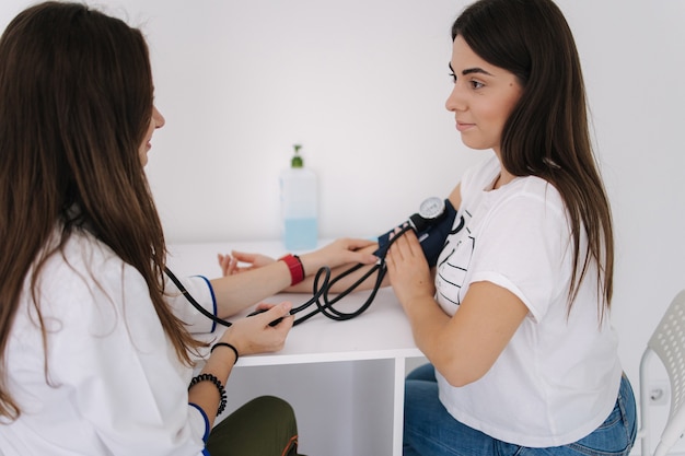 Femme médecin à l'aide d'un sphygmomanomètre avec stéthoscope vérifiant la pression artérielle d'un patient dans le