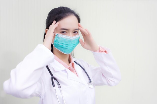 Femme médecin asiatique assise dans la salle d'examen portant un masque et réfléchissant aux soins de santé