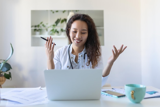 Femme médecin asiatique ayant une thérapie en ligne avec ses patients leur donnant des conseils tout en utilisant la télémédecine comme une nouvelle norme pendant l'épidémie de pandémie de COVID19