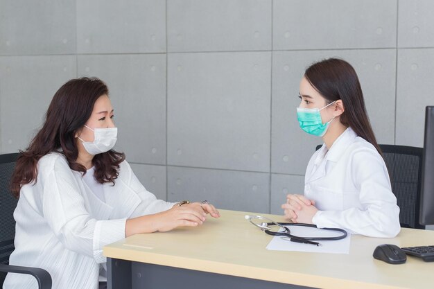 Une femme médecin asiatique parle avec son patient pendant qu'elle porte un masque médical à l'hôpital