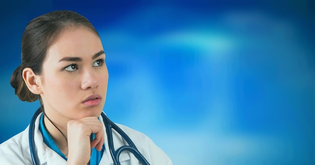 Femme médecin asiatique portant un stéthoscope avec la main sur le menton sur fond dégradé bleu