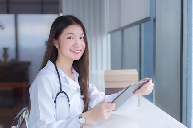 Une femme médecin asiatique vêtue d'une blouse médicale blanche est assise sur une chaise à la bibliothèque de l'hôpital