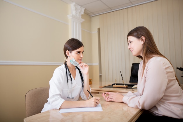 Femme médecin assis au bureau du bureau et écrivant une ordonnance au patient.