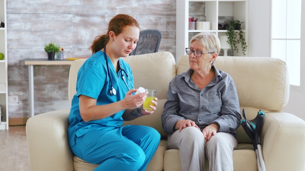 Femme médecin assise sur un canapé avec une femme âgée en maison de retraite lui donnant des pilules quotidiennes.