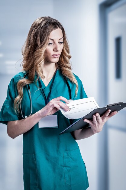 Femme médecin en blouse blanche avec stéthoscope et porte-papier bleu dans les mains debout isolé sur fond blanc