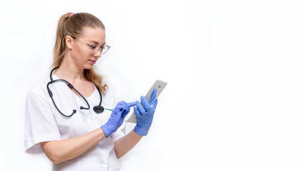 Femme médecin en blouse blanche avec stéthoscope tient une tablette dans les mains remplit la carte électronique du patient technologies modernes en médecine réception en ligne traitement virtuel service d'ambulance à distance