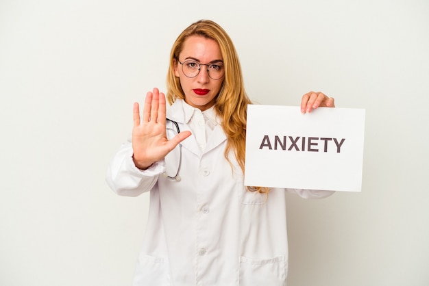 Femme médecin caucasien tenant une pancarte d'anxiété isolée sur fond blanc, debout avec la main tendue montrant un panneau d'arrêt, vous empêchant.