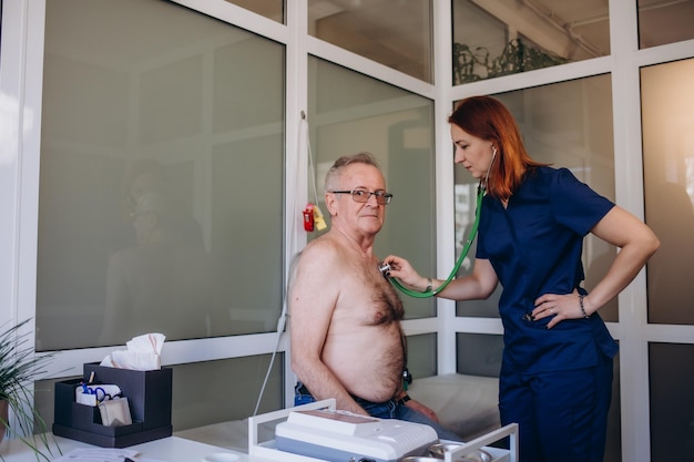 Une femme médecin caucasienne bienveillante utilise un phonendoscope pour examiner la fréquence cardiaque d'un patient masculin mature lors d'une consultation à l'hôpital
