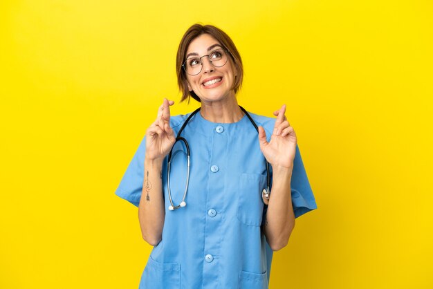 Femme médecin chirurgien isolée sur fond jaune avec croisement de doigts