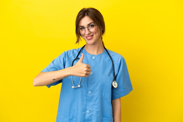 Femme médecin chirurgien isolée sur fond jaune donnant un geste du pouce vers le haut