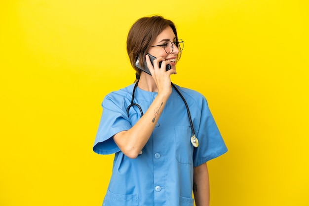 Femme médecin chirurgien isolée sur fond jaune gardant une conversation avec le téléphone portable avec quelqu'un
